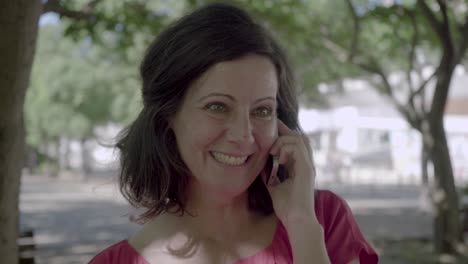 Mujer-Sonriente-De-Mediana-Edad-Hablando-Por-Teléfono-Inteligente-En-El-Parque